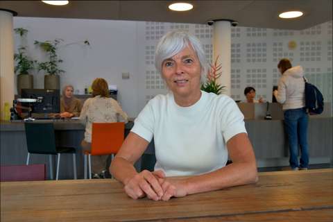 Caroline Timmermans zit aan tafel in woonwinkel Tilburg met mensen op de achtergrond en kijkt in de camera